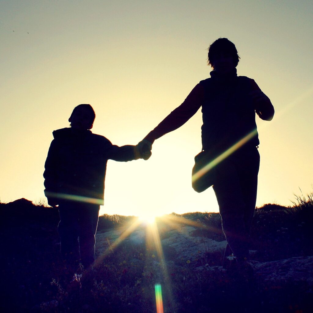 a parent and child holding hands with the sun behind them